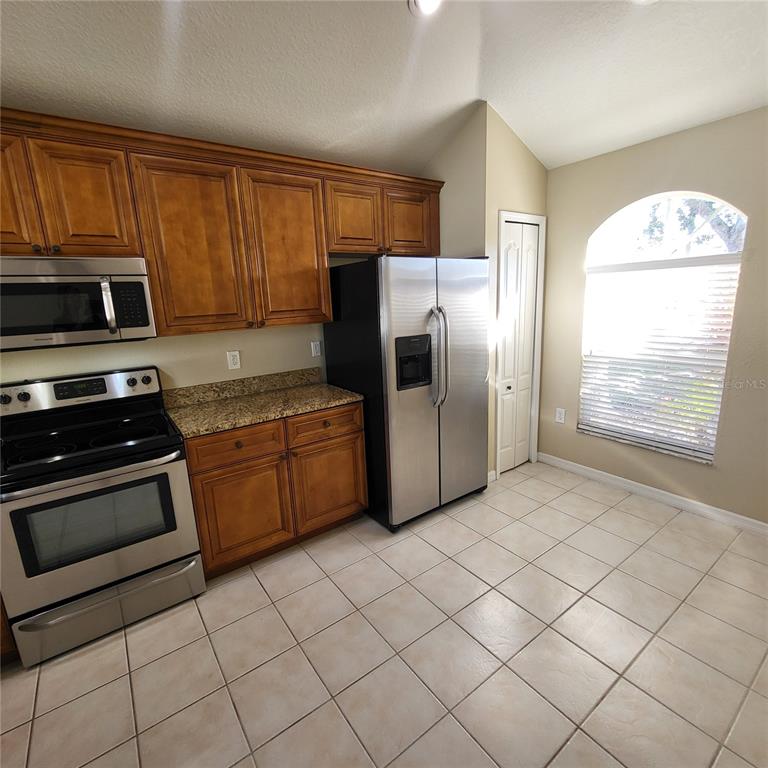 A kitchen features wood cabinets, granite countertops, stainless steel appliances, and a tiled floor — 25903 BLOOMSBURY COURT, LAND O LAKES, FL