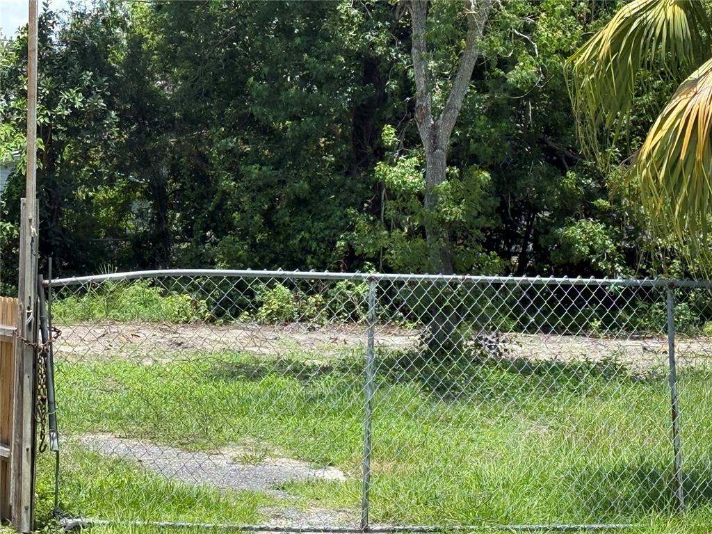 A chain-link fence encloses a grassy lot with trees and vegetation in the background — 7018 S 51ST AVENUE, TAMPA, FL