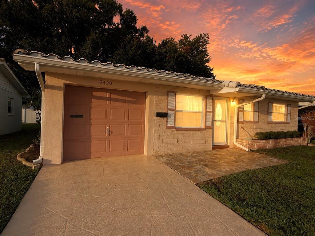 A single-story house with a tan brick facade, a garage, and a paved front patio — 5420 PALM CREST COURT N, PINELLAS PARK, FL