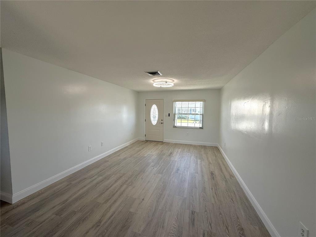 An empty living room features light wood-look flooring, white walls, and a central ceiling light — 5420 PALM CREST COURT N, PINELLAS PARK, FL