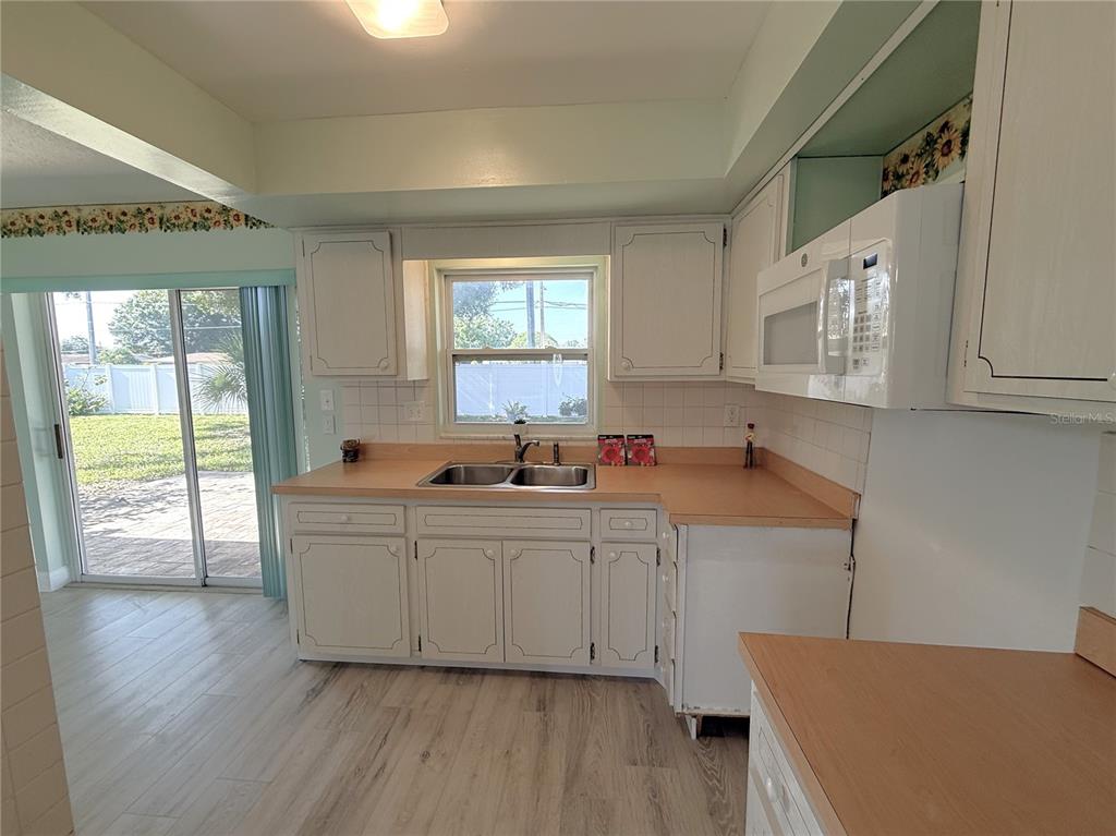 A kitchen features white cabinets, laminate countertops, a double sink, and a sliding glass door — 5420 PALM CREST COURT N, PINELLAS PARK, FL