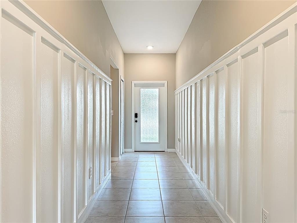 A narrow hallway features white board-and-batten wall paneling, tile flooring, and a glass-paneled front door — 4449 ETERNAL PRINCE DRIVE, SUN CITY CENTER, FL