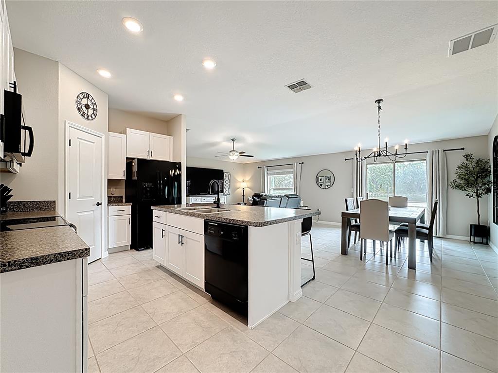 A kitchen with white cabinets and a granite island opens into a dining area — 4449 ETERNAL PRINCE DRIVE, SUN CITY CENTER, FL