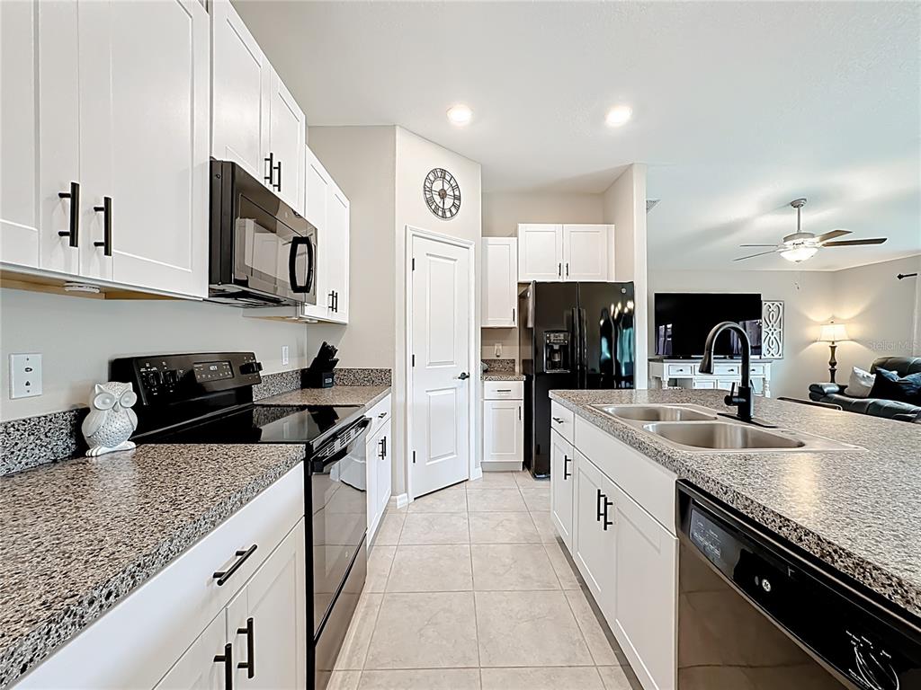 A kitchen features white cabinets, granite countertops, black appliances, and a central island with a sink — 4449 ETERNAL PRINCE DRIVE, SUN CITY CENTER, FL