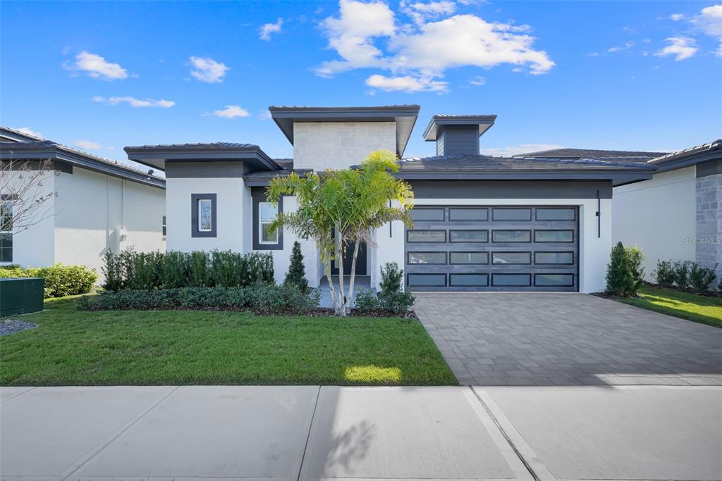 A modern single-story house with a stone facade, dark trim, and a multi-panel garage door — 3044 KENSINGTON AVENUE, DAVENPORT, FL