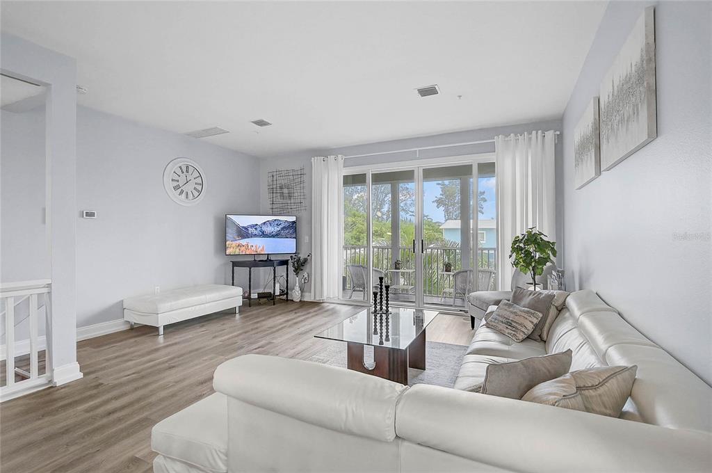 A bright living room features light wood flooring, a white sectional sofa, and sliding glass doors — 508 FOREST WAY UNIT 508, LONGBOAT KEY, FL