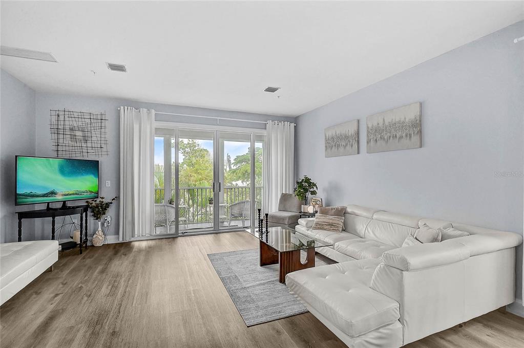 A living room features light wood flooring, a white sectional sofa, and sliding glass balcony doors — 508 FOREST WAY UNIT 508, LONGBOAT KEY, FL