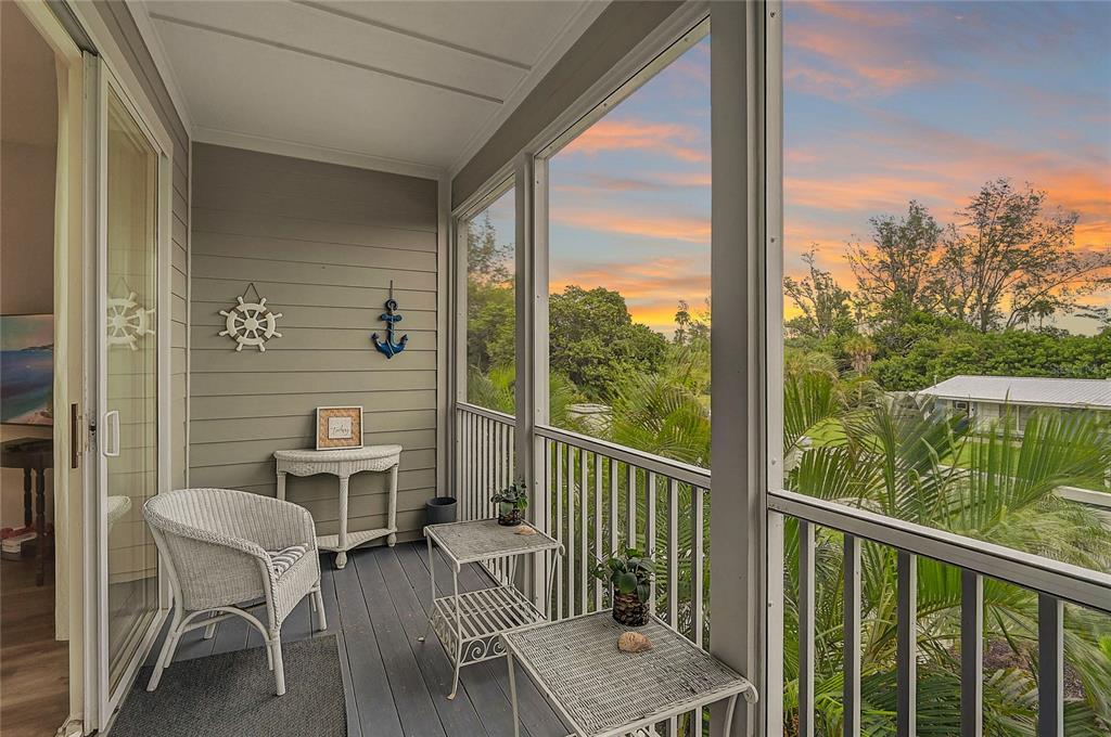 A screened-in balcony features wicker furniture, nautical wall decor, and views of tropical greenery — 508 FOREST WAY UNIT 508, LONGBOAT KEY, FL