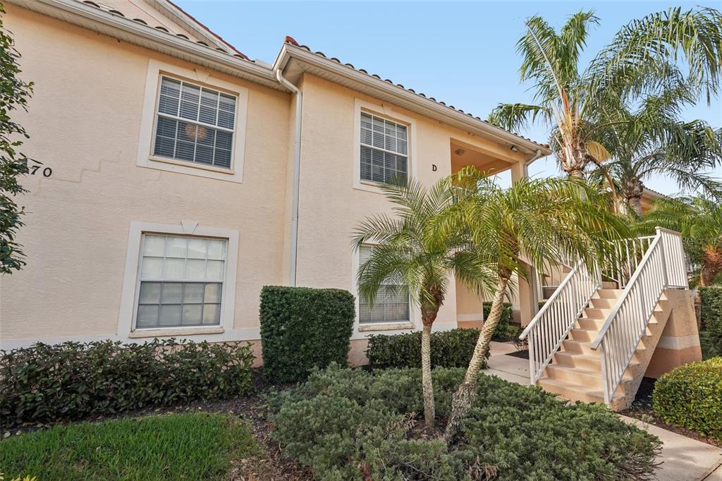 A two-story tan stucco apartment building features a staircase leading to an upper-level balcony — 4270 VICENZA DRIVE UNIT D40, VENICE, FL