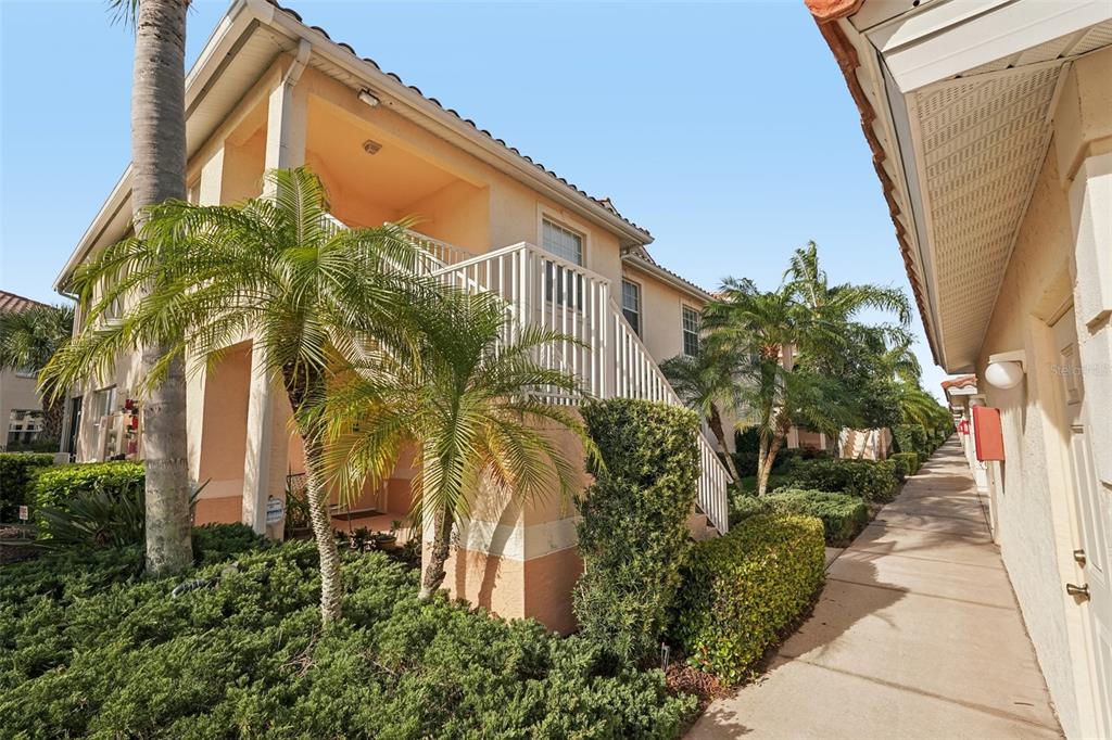 A two-story apartment building exterior with a palm tree, staircase, and a concrete walkway — 4270 VICENZA DRIVE UNIT D40, VENICE, FL