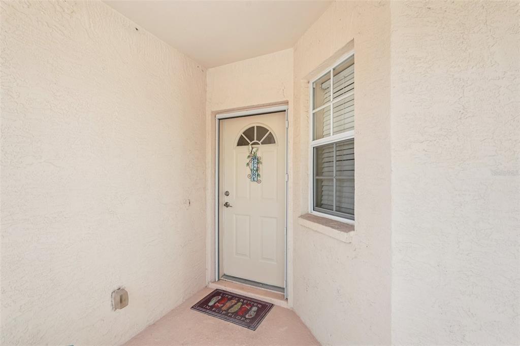A beige stucco entryway features a white front door with a window and a doormat — 4270 VICENZA DRIVE UNIT D40, VENICE, FL
