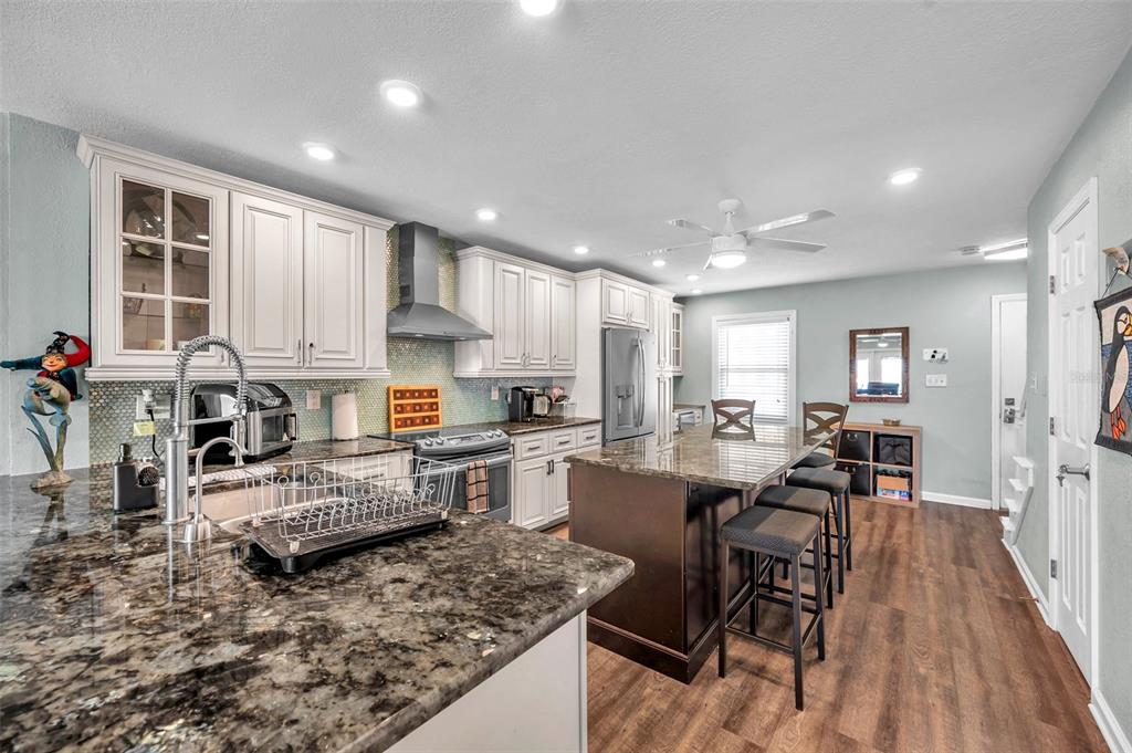A kitchen features white cabinets, dark granite countertops, a center island, and wood-look flooring — 4768 COQUINA KEY DRIVE SE, ST PETERSBURG, FL
