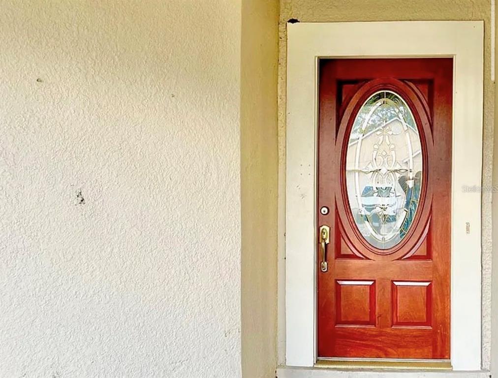 A red front door with an oval glass insert is set in a white frame — 13158 ODYSSEY LAKE WAY, ORLANDO, FL