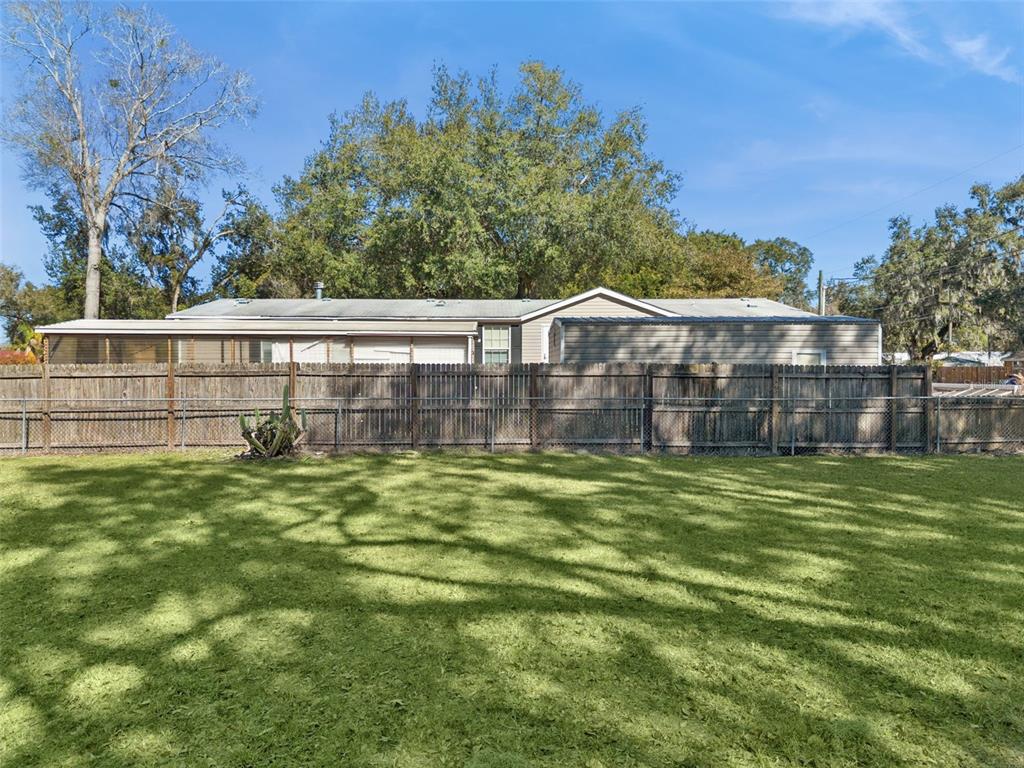 A wide backyard features a large lawn, a wooden fence, and a single-story house — 1724 EVERGREEN STREET, KISSIMMEE, FL