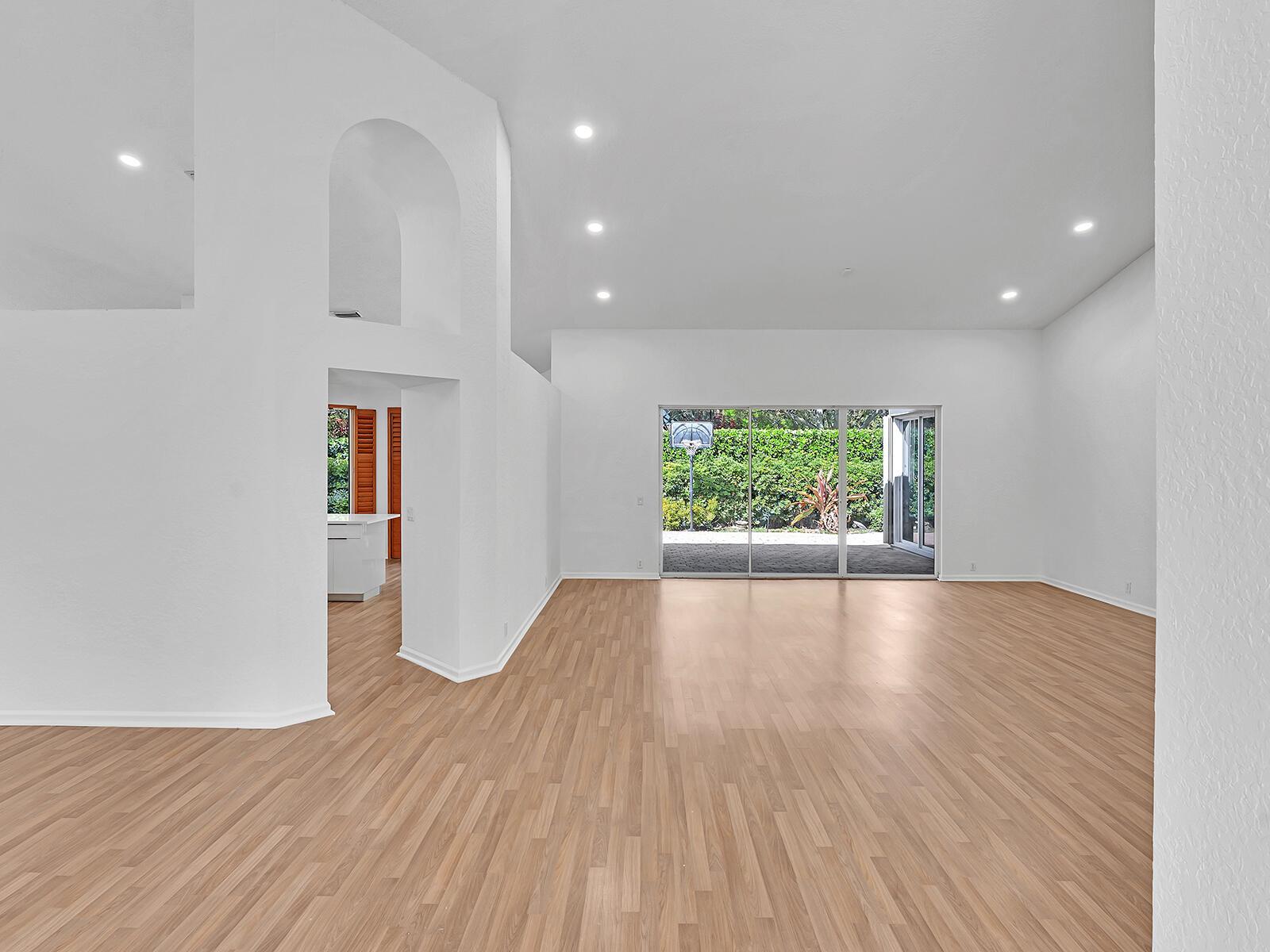 An empty living room features light wood-look flooring, white walls, recessed lighting, and sliding glass doors — 3420 Washington Lane, Cooper City FL 33026, COOPER CITY, FL