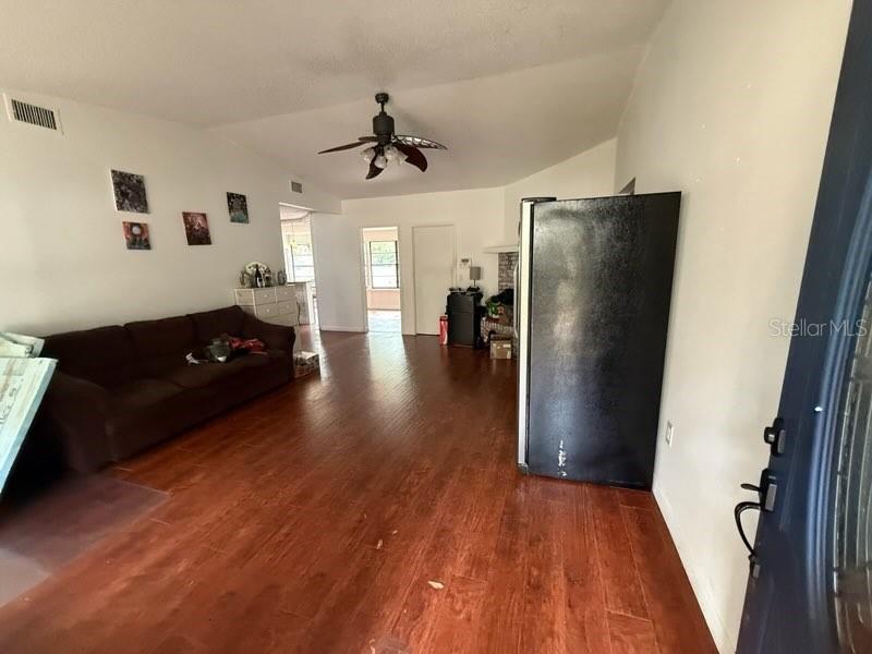 A living room with wood-look flooring, a brown sofa, and a black refrigerator — 684 STRATFORD DRIVE, DELAND, FL