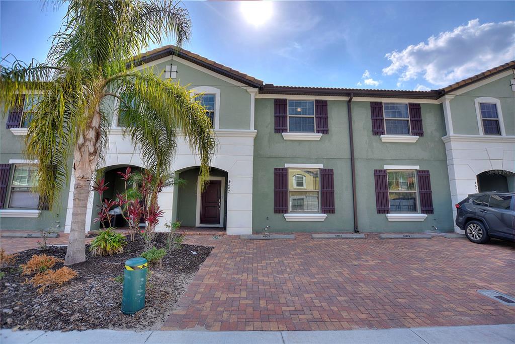 A multi-story townhouse exterior with a brick driveway, palm tree, and green stucco facade — 4607 TERRASONESTA DRIVE, DAVENPORT, FL