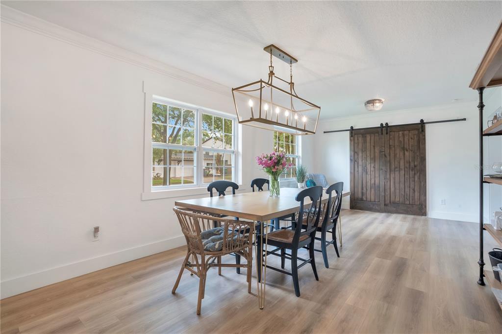 A dining room features a wooden table, mixed seating, a rectangular chandelier, and sliding barn doors — 2702 PARKLAND DRIVE, WINTER PARK, FL