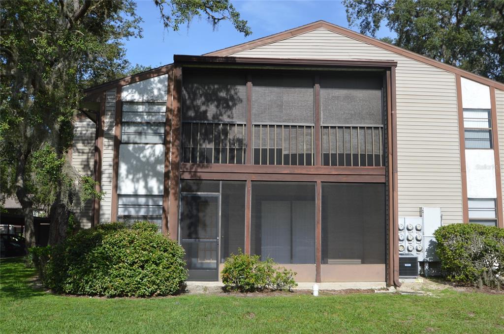 A two-story building exterior features a screened-in porch, tan siding, and surrounding landscaping — 12010 PROCTOR LOOP UNIT 4, NEW PORT RICHEY, FL