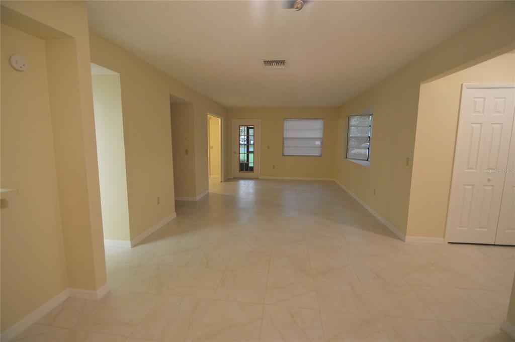 An empty living room with light-colored tile flooring, beige walls, and a glass-paneled entry door — 12010 PROCTOR LOOP UNIT 4, NEW PORT RICHEY, FL