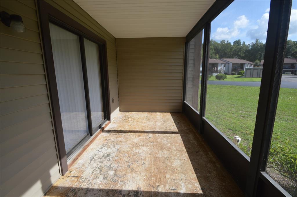 A screened-in porch with a weathered concrete floor and sliding glass doors — 12010 PROCTOR LOOP UNIT 4, NEW PORT RICHEY, FL