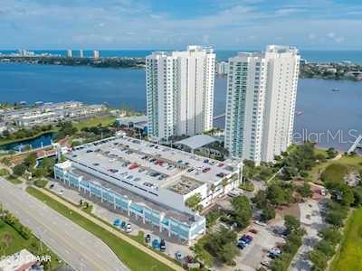 An aerial view shows two tall residential towers next to a large parking garage — 235 RIVERSIDE DRIVE, DAYTONA BEACH, FL