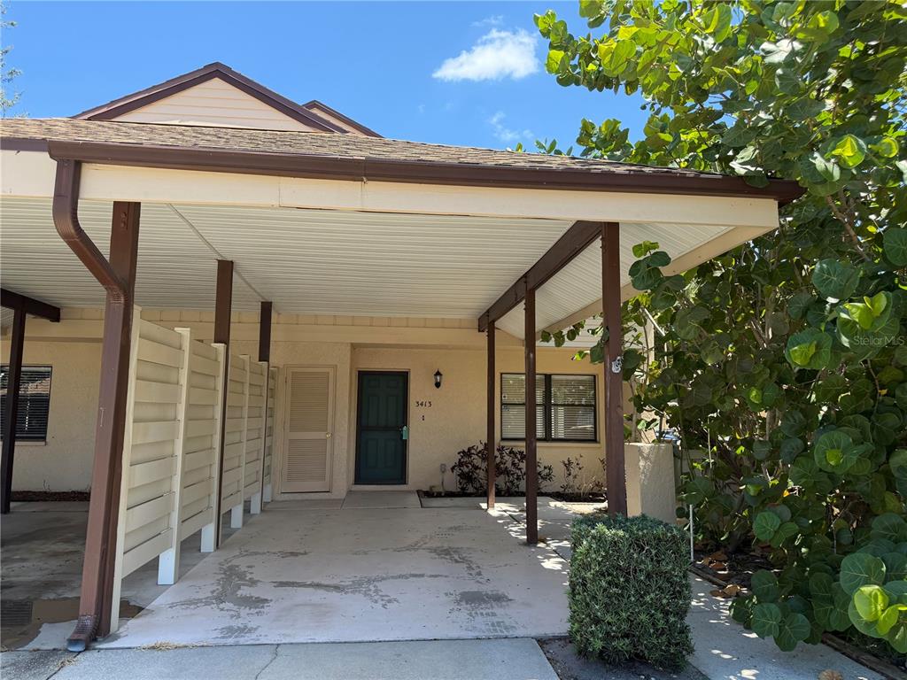 A beige house exterior features a covered carport, a front door, and a small bush — 3413 51ST AVENUE CIRCLE W UNIT 205, BRADENTON, FL