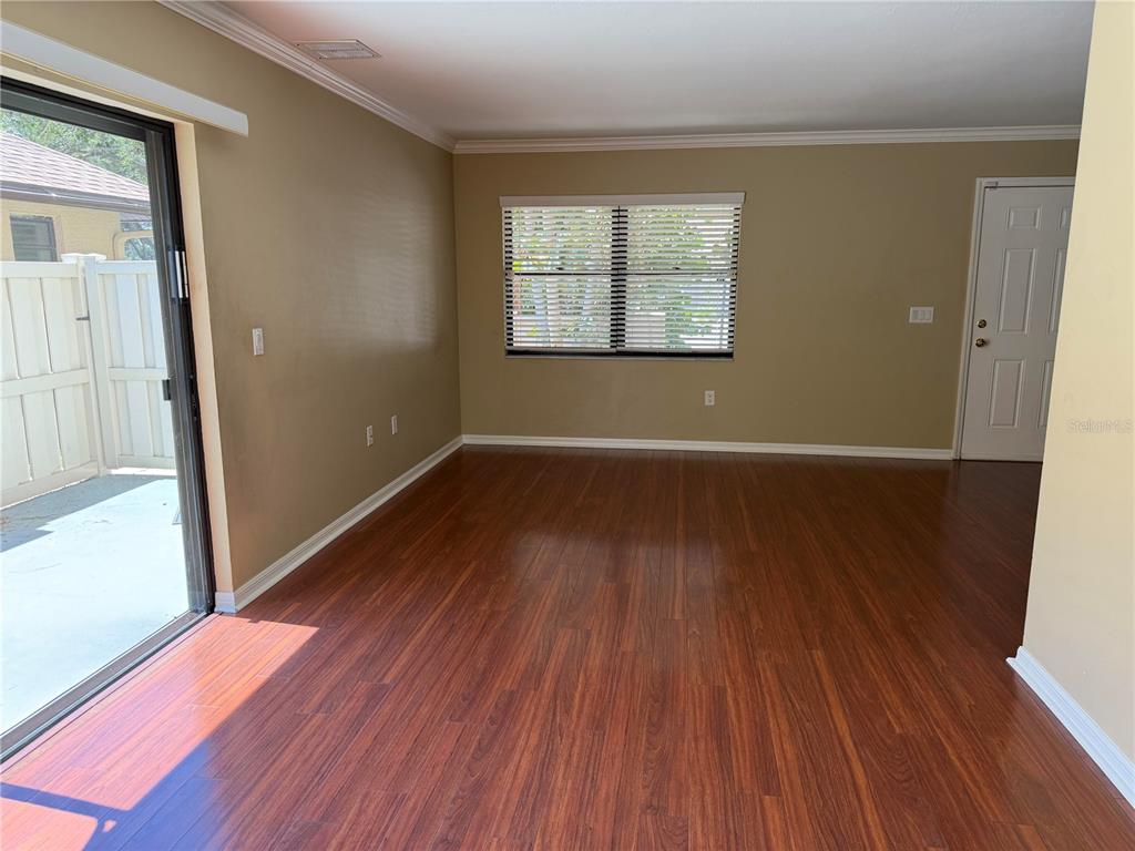 An empty room features wood-look flooring, tan walls, a sliding glass door, and a window — 3413 51ST AVENUE CIRCLE W UNIT 205, BRADENTON, FL