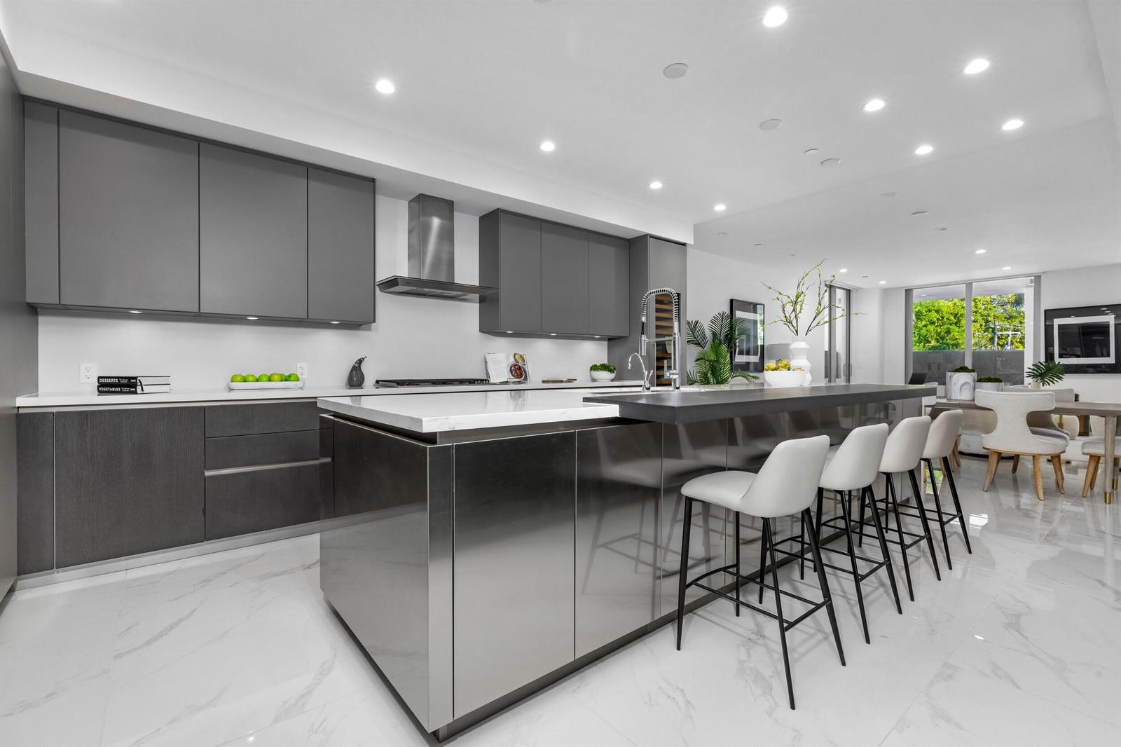 A modern kitchen features dark gray cabinetry, a stainless steel island, and white marble flooring — 495 E Royal Palm Road # 201, Boca Raton FL 33432, BOCA RATON, FL