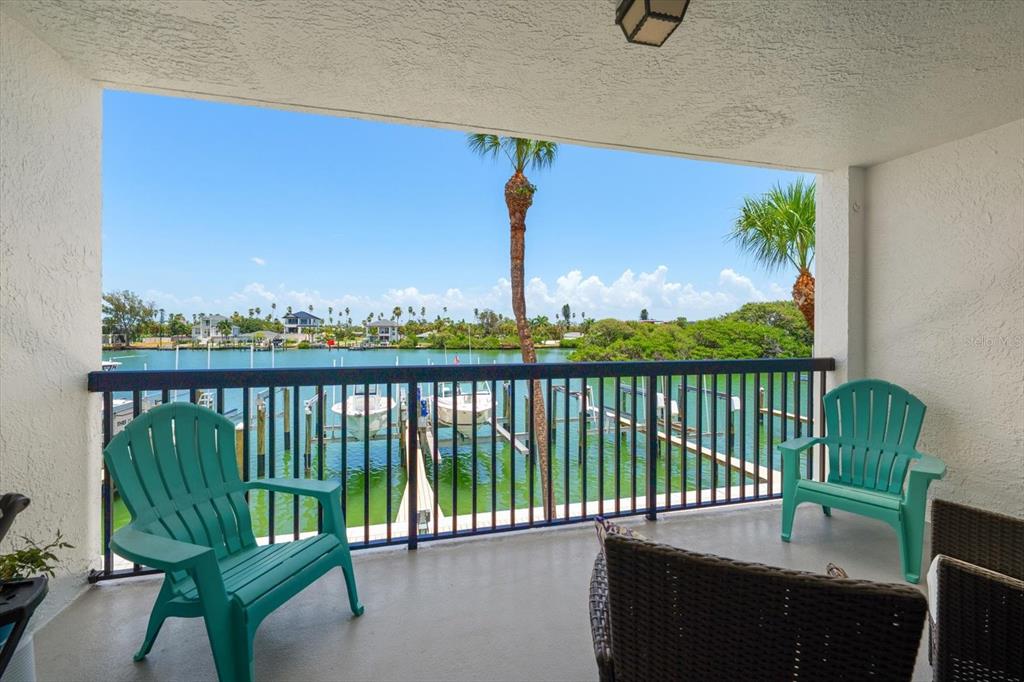 A covered balcony features two teal Adirondack chairs overlooking a canal with boat docks — 3111 PASS A GRILLE WAY UNIT 110, ST PETERSBURG, FL