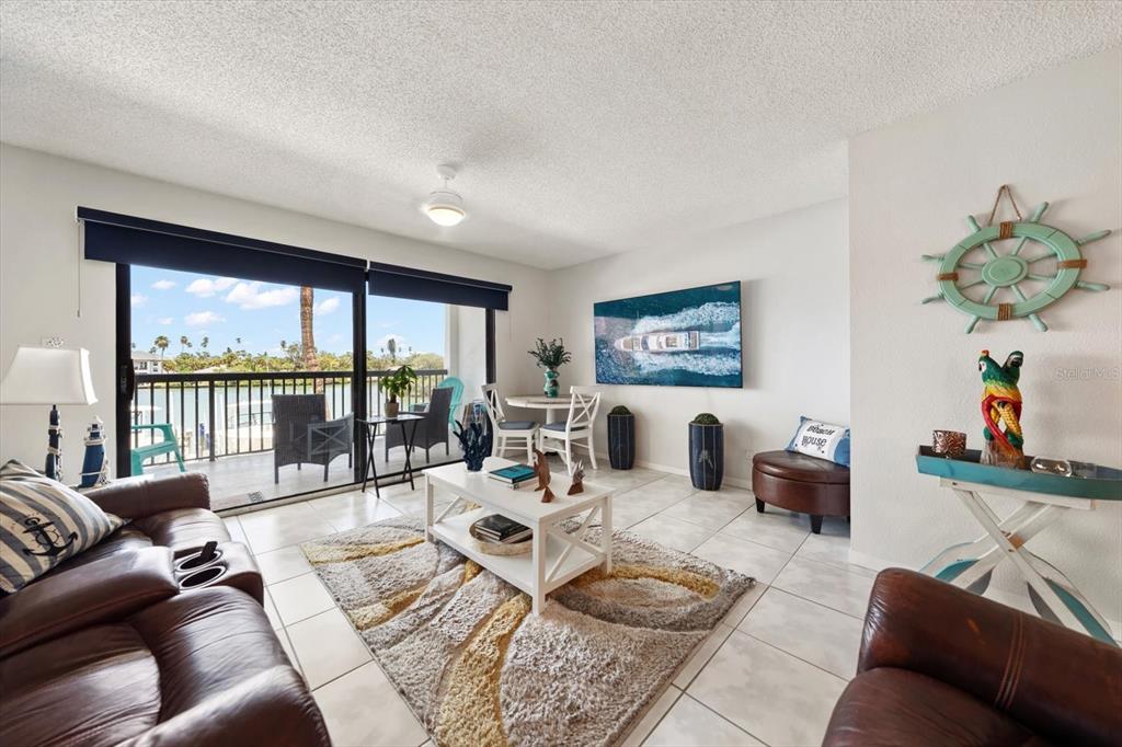 A living room with tile floors, a brown leather sofa, and a balcony overlooking water — 3111 PASS A GRILLE WAY UNIT 110, ST PETERSBURG, FL