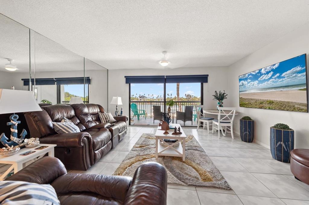 A living room features brown leather furniture, a mirrored wall, and a sliding door to a balcony — 3111 PASS A GRILLE WAY UNIT 110, ST PETERSBURG, FL