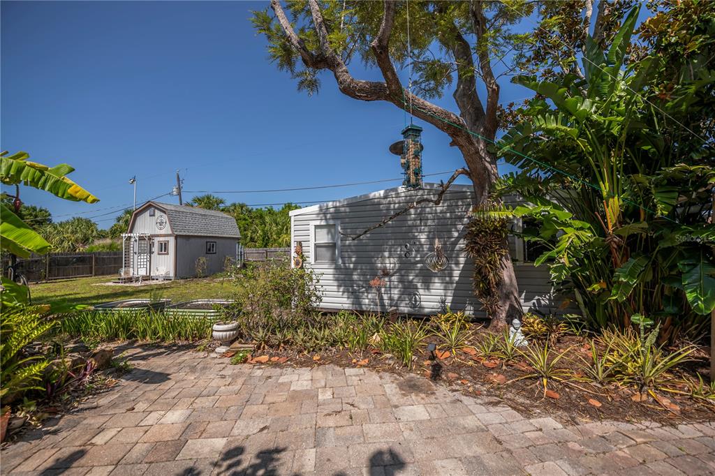 A backyard features a paved patio, a small shed, and a mobile home under trees — 3017 CHICORY TERRACE, PUNTA GORDA, FL