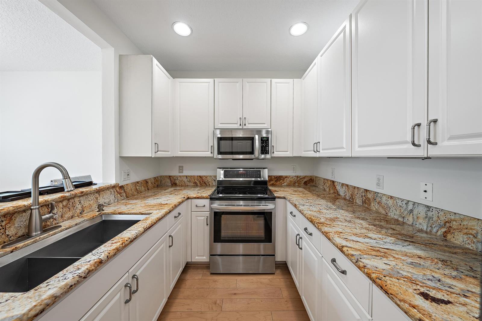 A kitchen features white cabinets, granite countertops, stainless steel appliances, and light wood flooring — 4316 Blowing Point Place, Jupiter FL 33458, JUPITER, FL