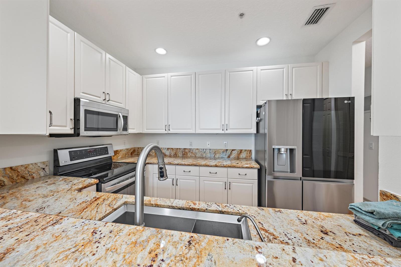 A kitchen features white cabinets, granite countertops, stainless steel appliances, and a double-basin sink — 4316 Blowing Point Place, Jupiter FL 33458, JUPITER, FL