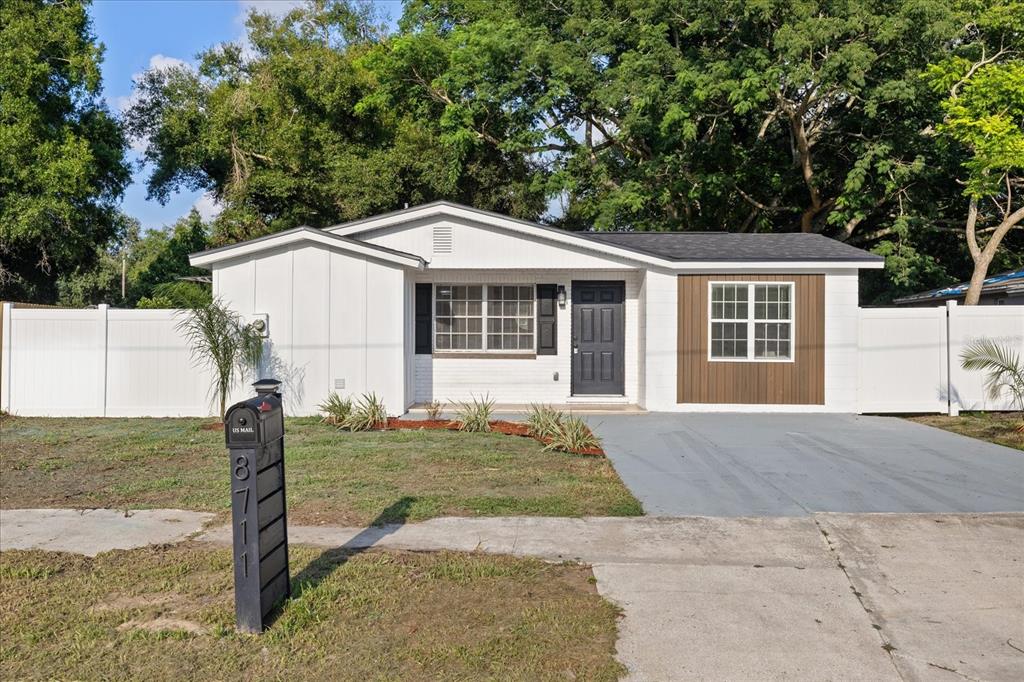 A single-story white house with a brown accent wall, dark door, and a white fence — 8711 N RIVER FOREST CIRCLE, TAMPA, FL