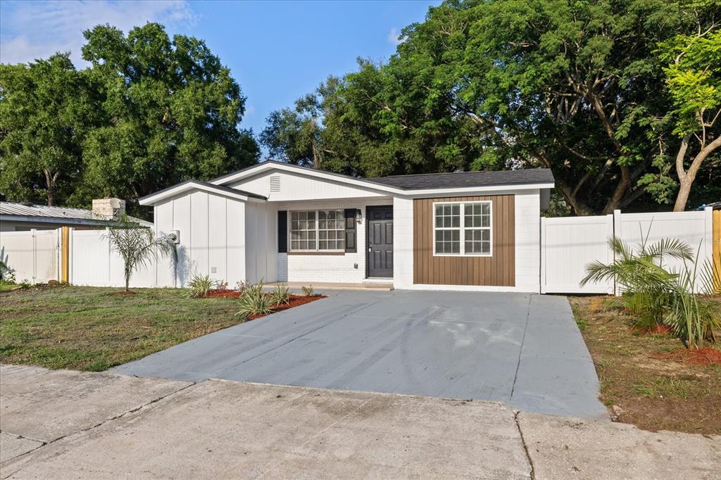 A single-story house with white siding, a brown accent wall, and a gray concrete driveway — 8711 N RIVER FOREST CIRCLE, TAMPA, FL