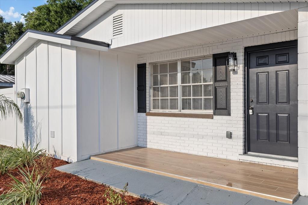 A white brick house exterior features a front porch with wood-look tile and black accents — 8711 N RIVER FOREST CIRCLE, TAMPA, FL