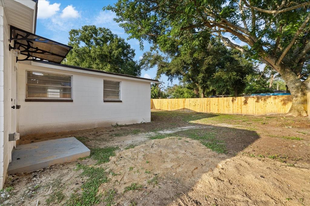 A white concrete block house exterior with a small patio and a wooden privacy fence — 8711 N RIVER FOREST CIRCLE, TAMPA, FL