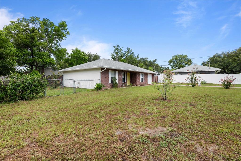A single-story brick and white house with a chain-link fence in a grassy yard — 5435 TANGERINE DRIVE, ZEPHYRHILLS, FL