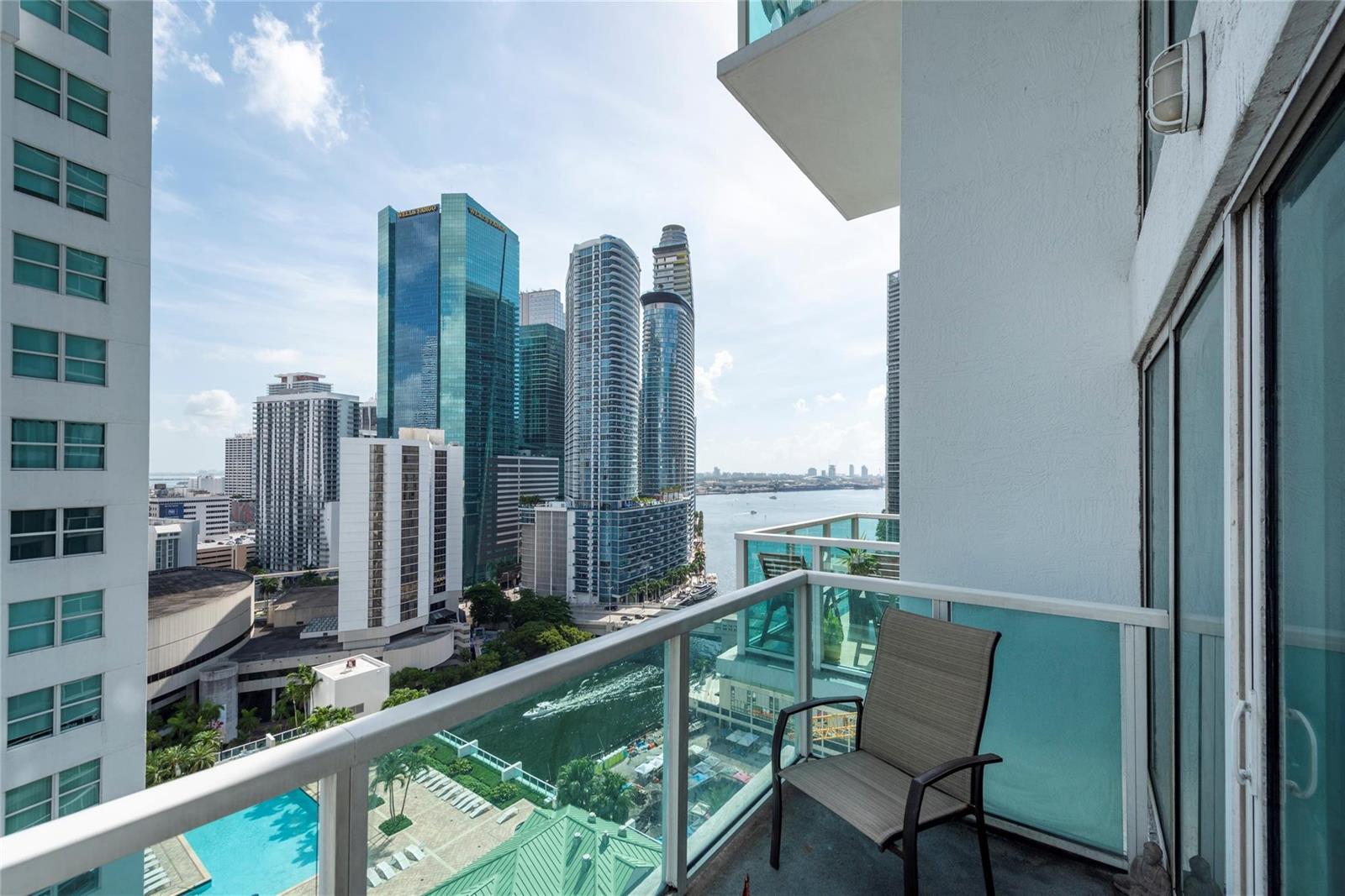A balcony with a chair overlooks a city skyline, a river, and a swimming pool — 41 SE 5th Street # 1315, Miami FL 33131, MIAMI, FL