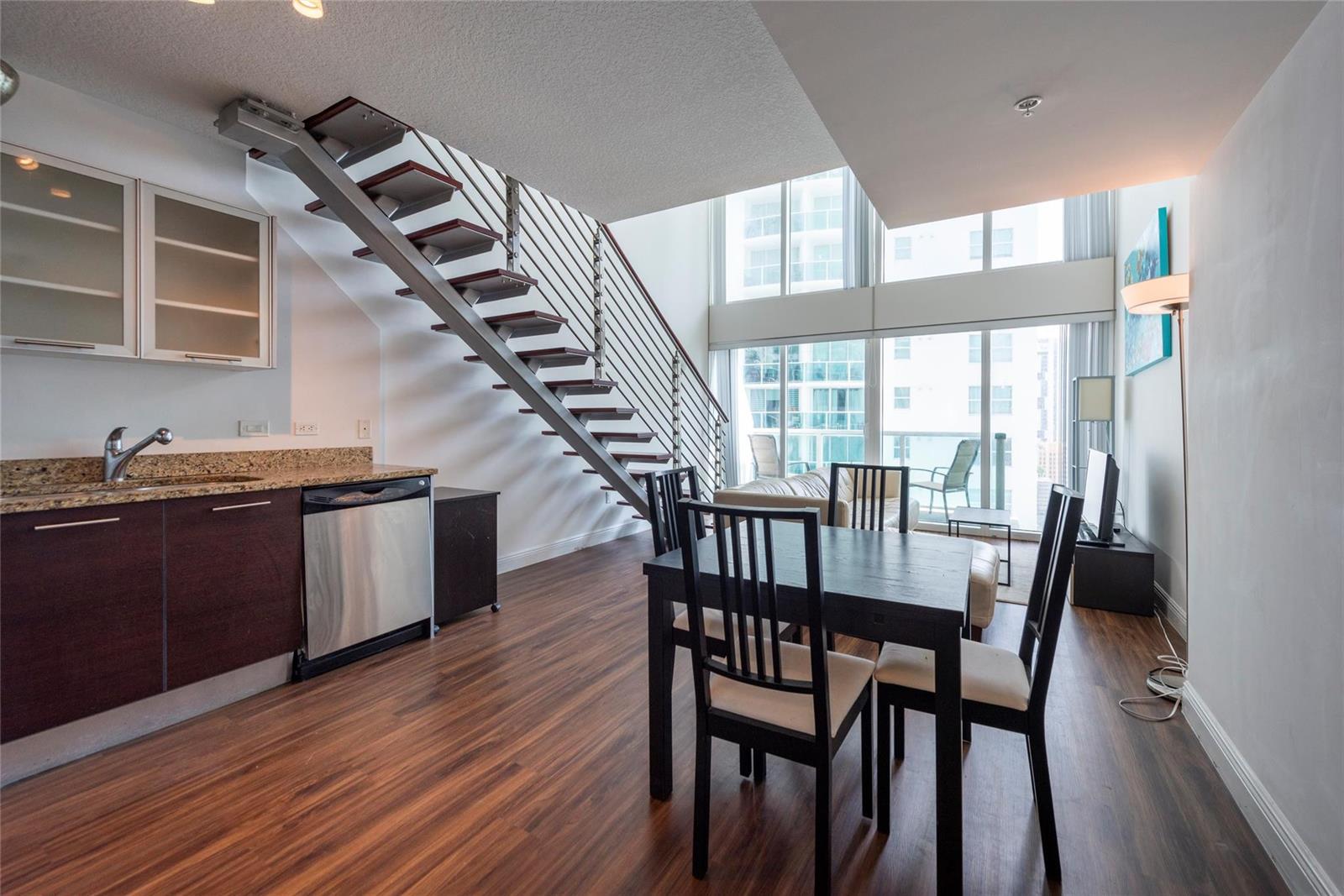 A modern kitchen and dining area features a floating staircase and floor-to-ceiling windows — 41 SE 5th Street # 1315, Miami FL 33131, MIAMI, FL