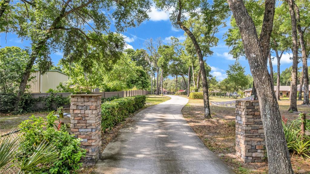 A concrete driveway leads through stone pillars toward a wooded property with mature trees — 721 MCGREGOR ROAD, DELAND, FL