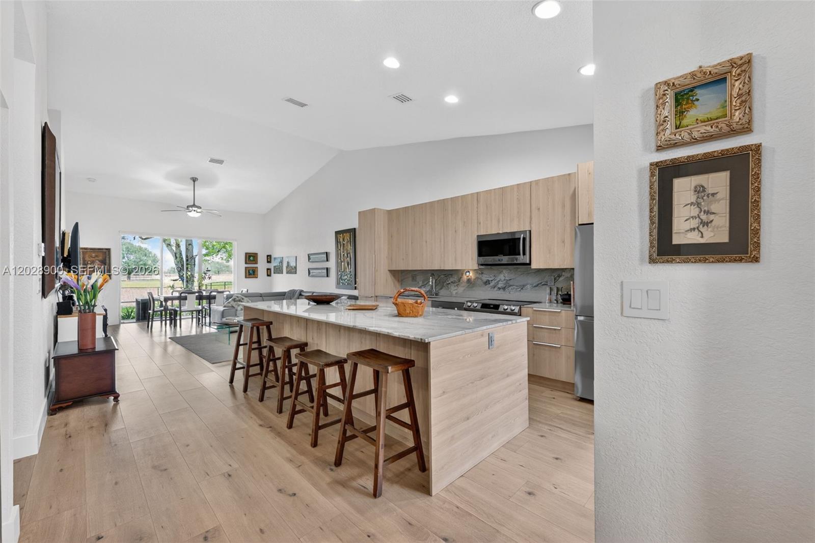 A modern kitchen features light wood cabinets, a marble island with barstools, and vaulted ceilings — 2411 Aragon Blvd # 2, Sunrise FL 33322, SUNRISE, FL
