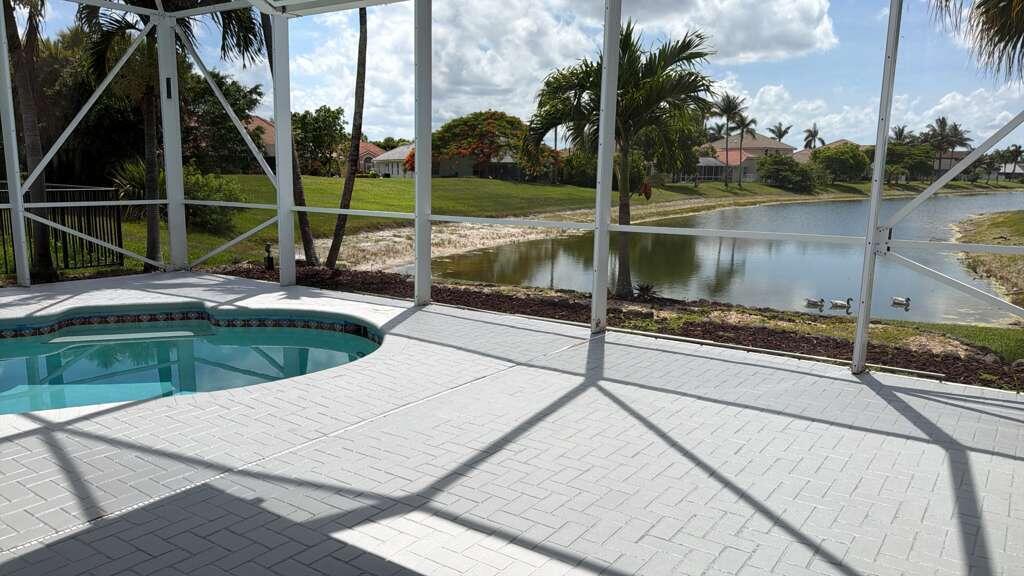 A screened-in patio features a small pool, light-colored pavers, and a view of a lake — 22257 Collington Drive, Boca Raton FL 33428, BOCA RATON, FL