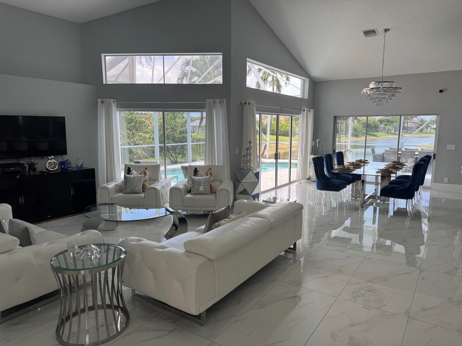 A spacious living and dining area with white leather furniture, marble floors, and pool views — 22257 Collington Drive, Boca Raton FL 33428, BOCA RATON, FL