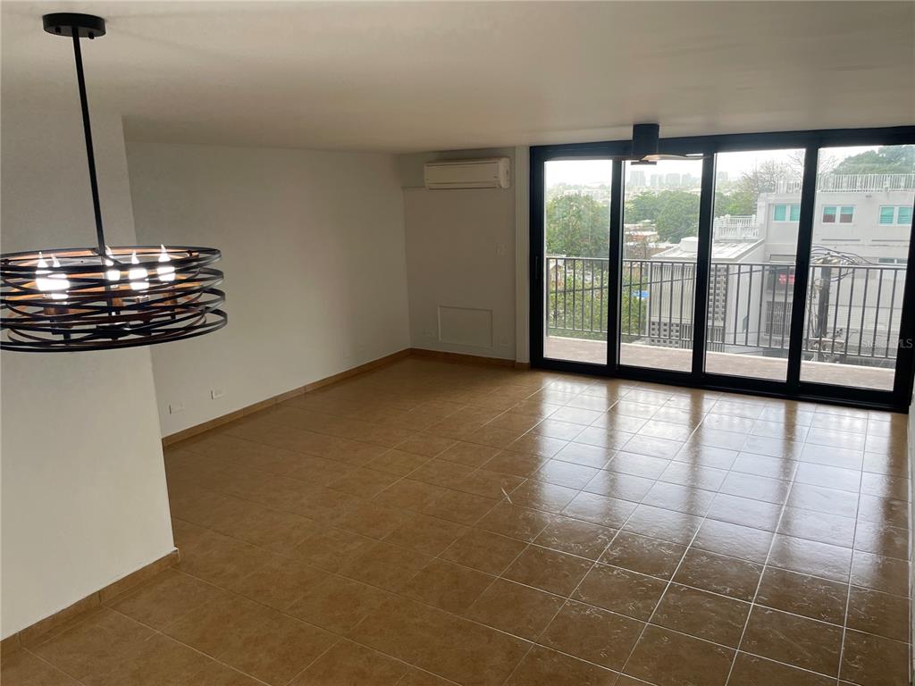An empty room features tan tile flooring, a modern pendant light, and sliding glass balcony doors — 364 CALLE SAN JORGE UNIT 3G, SAN JUAN, PR