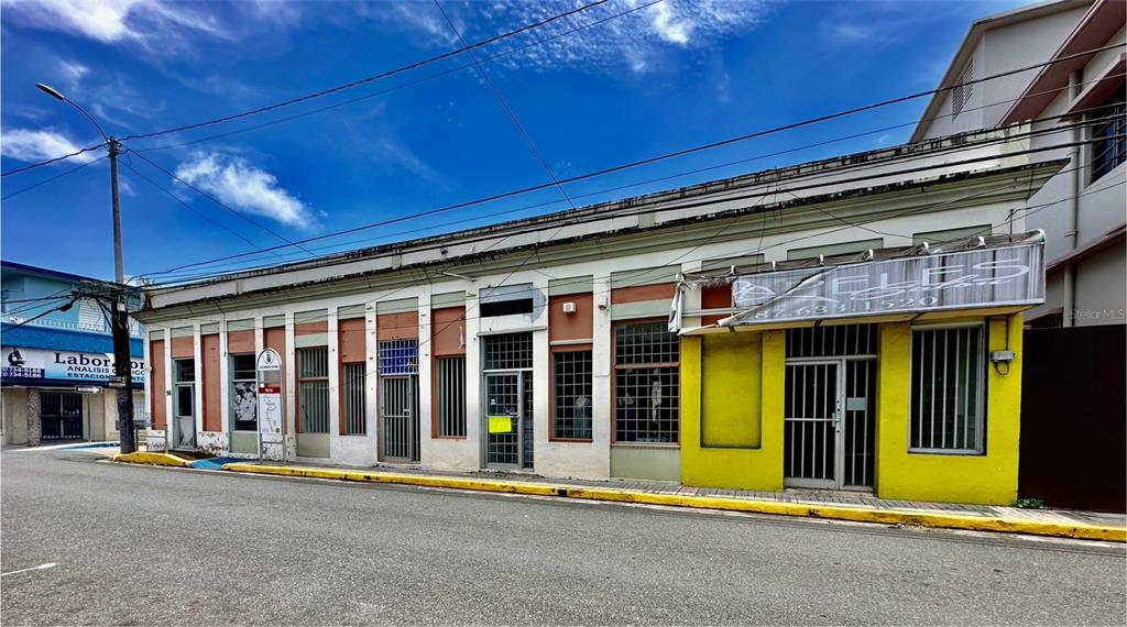 A street-level view of a commercial building with multiple storefronts and a yellow facade — 58 MUÑOZ RIVERA ESQ CORCHADO, JUNCOS, PR
