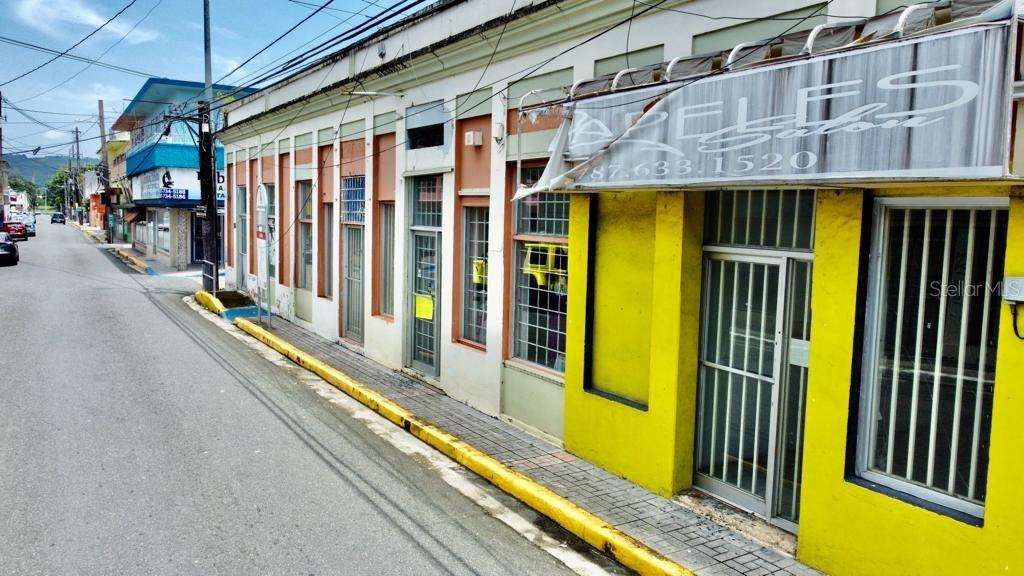 A street-level view of a commercial building with a yellow facade and metal security bars — 58 MUÑOZ RIVERA ESQ CORCHADO, JUNCOS, PR