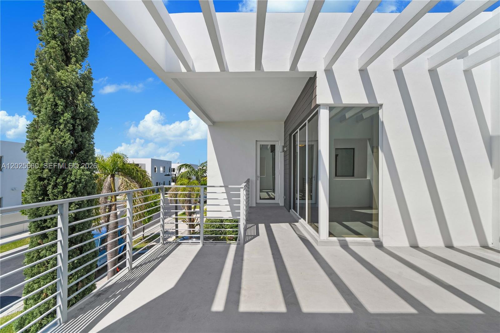 A modern balcony features a white pergola, metal railings, and glass doors overlooking a street — 9915 NW 75th St, Doral FL 33178, DORAL, FL